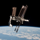 The international space station hovering in low earth orbit in front of a background of the earth and the deep black of space. A space shuttle is attached to one end of the station.